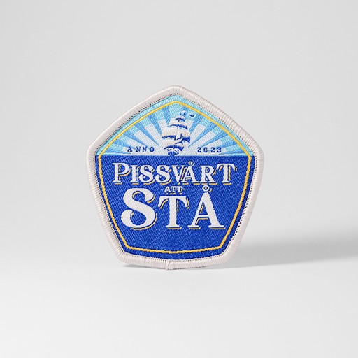 Blått tygmärke med texten "Pissvårt Att Stå"